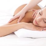 Total relaxation. Beautiful young woman lying on front and looking at camera while massage therapist massaging her shoulders