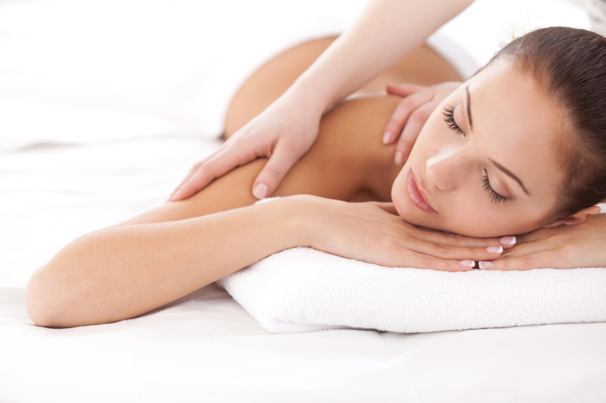 Total relaxation. Beautiful young woman lying on front and looking at camera while massage therapist massaging her shoulders